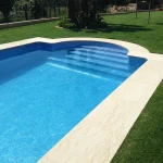 bazen plave boje vode sa bijelim rubnim kamenom i zelenom travom okolo