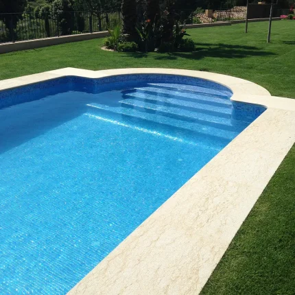 bazen plave boje vode sa bijelim rubnim kamenom i zelenom travom okolo